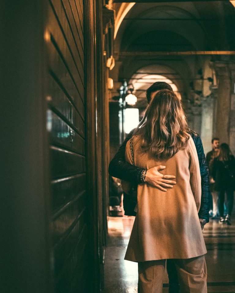 A couple shares an embrace in a warmly lit historic corridor, creating a romantic atmosphere.